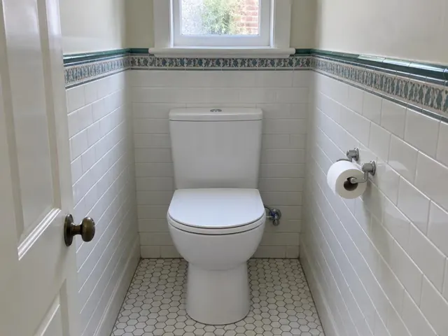 Clean white toilet in a tiled small bathroom with patterned border and window in Guildford