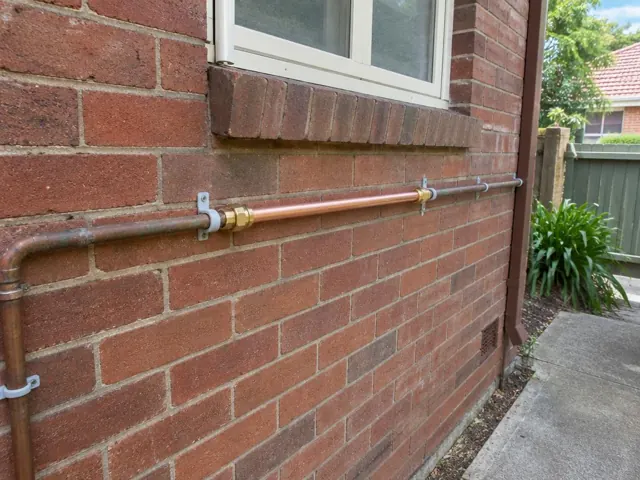 Repaired copper water pipe on a brick exterior wall below a window in Fairfield