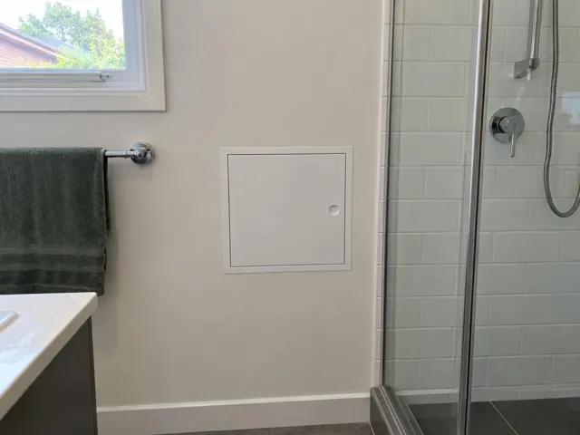Small access panel in a tiled bathroom wall beside a shower and towel rail in Guildford
